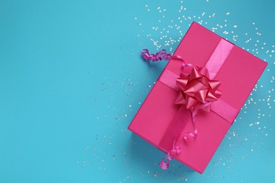 Pink gift box and shiny confetti on light blue background, top view. Space for text