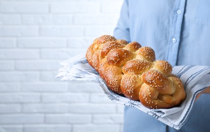 Photo of Closeup view of woman holding homemade braided bread near white brick wall, space for text. Traditional Shabbat challah