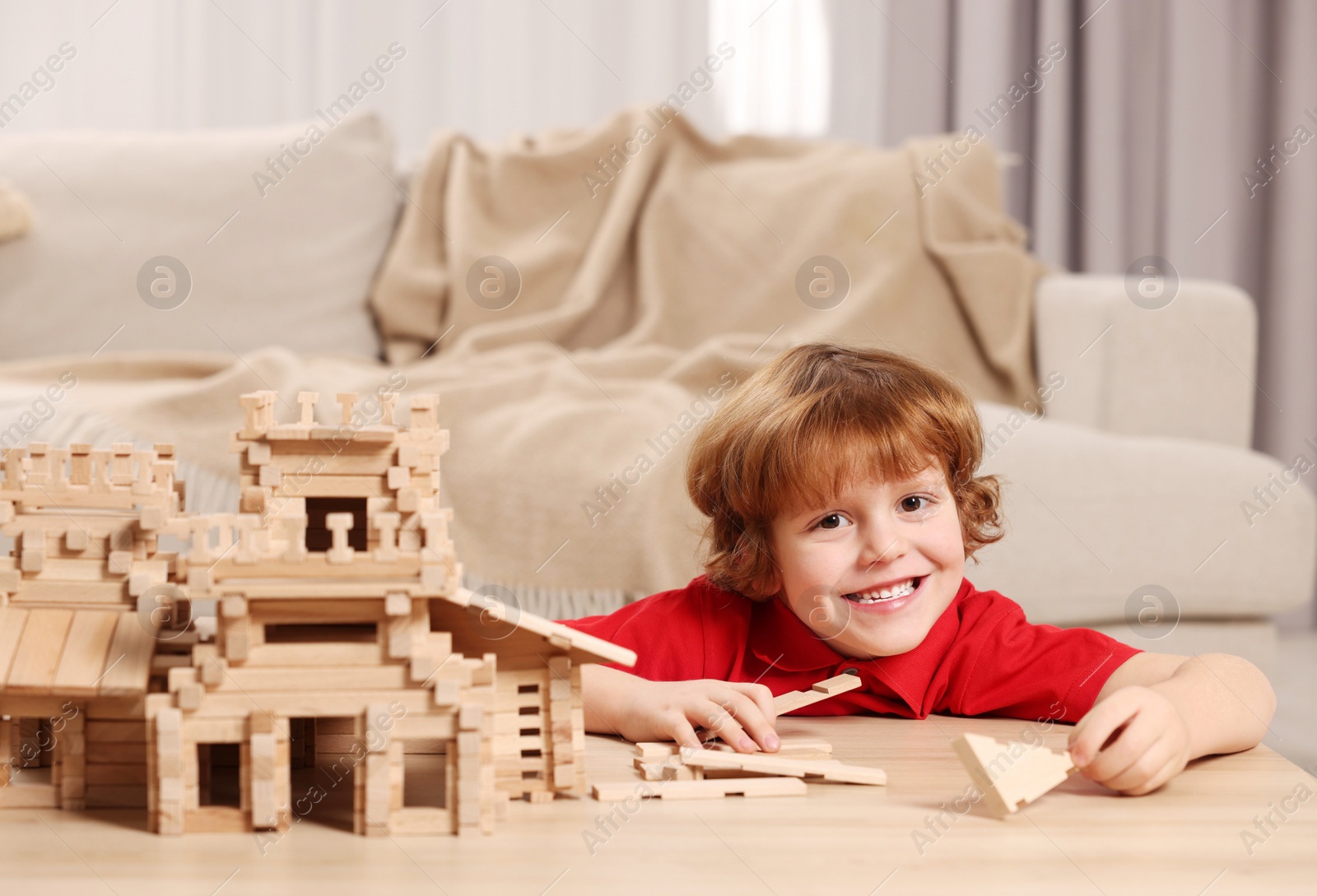 Photo of Cute little boy playing with wooden castle at table in room. Child's toy