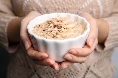 Photo of Woman holding bowl of quinoa porridge with banana and nuts, closeup
