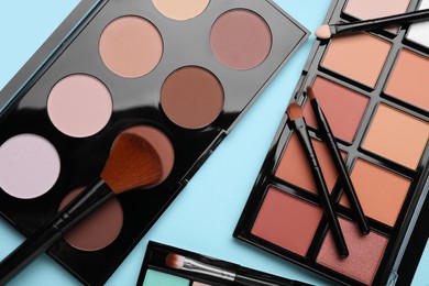 Photo of Colorful contouring palettes with brushes on light blue background, flat lay. Professional cosmetic product