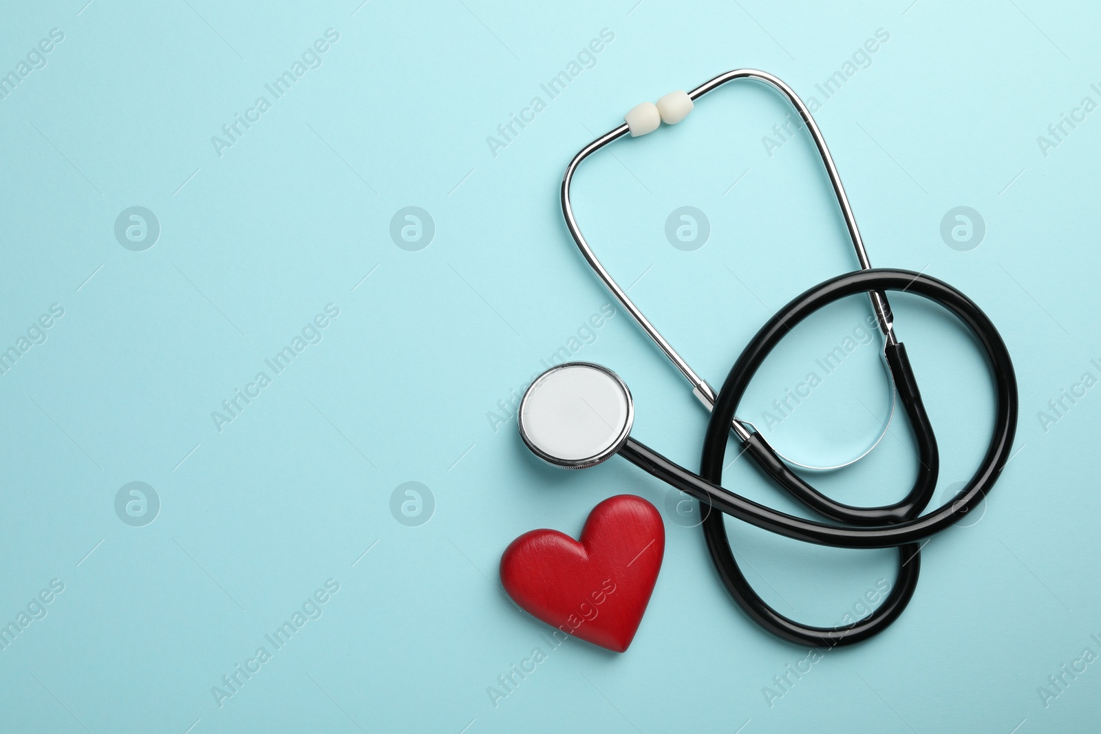 Photo of Stethoscope and red heart on light blue background, top view. Space for text