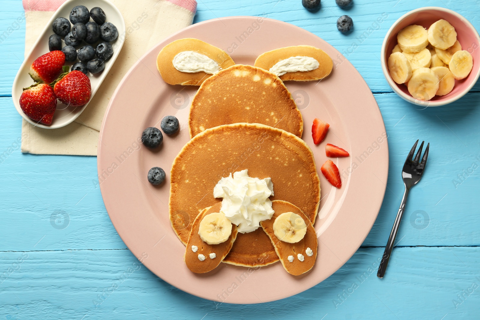 Photo of Creative serving for kids. Plate with cute bunny made of pancakes, berries, cream and banana on light blue wooden table, flat lay