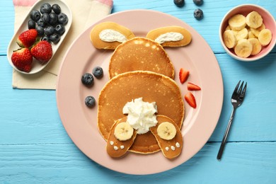 Photo of Creative serving for kids. Plate with cute bunny made of pancakes, berries, cream and banana on light blue wooden table, flat lay