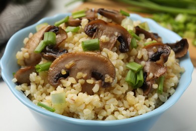 Photo of Delicious bulgur with mushrooms and green onion in bowl on table, closeup