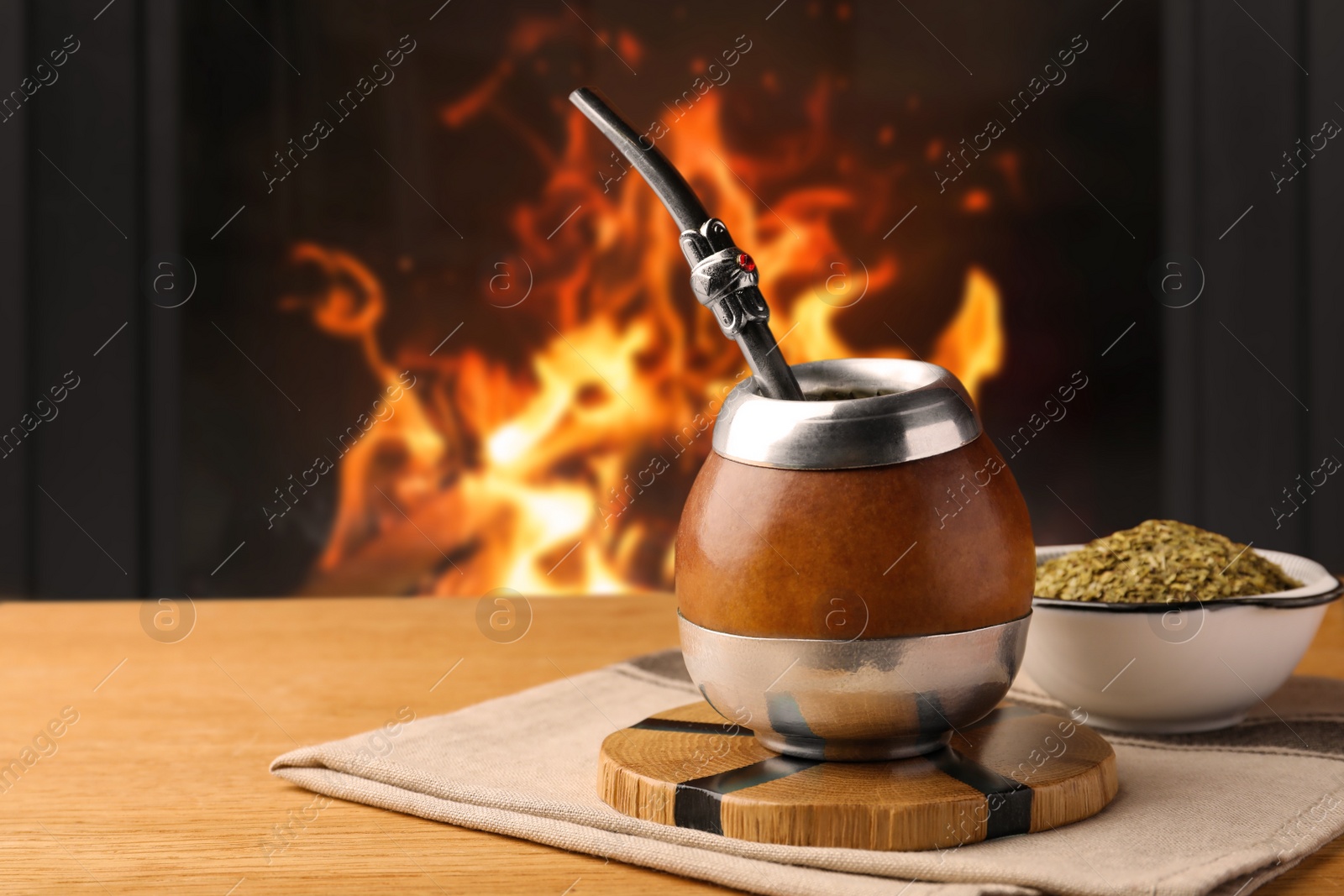 Image of Calabash with mate tea and bombilla on wooden table near fireplace. Space for text