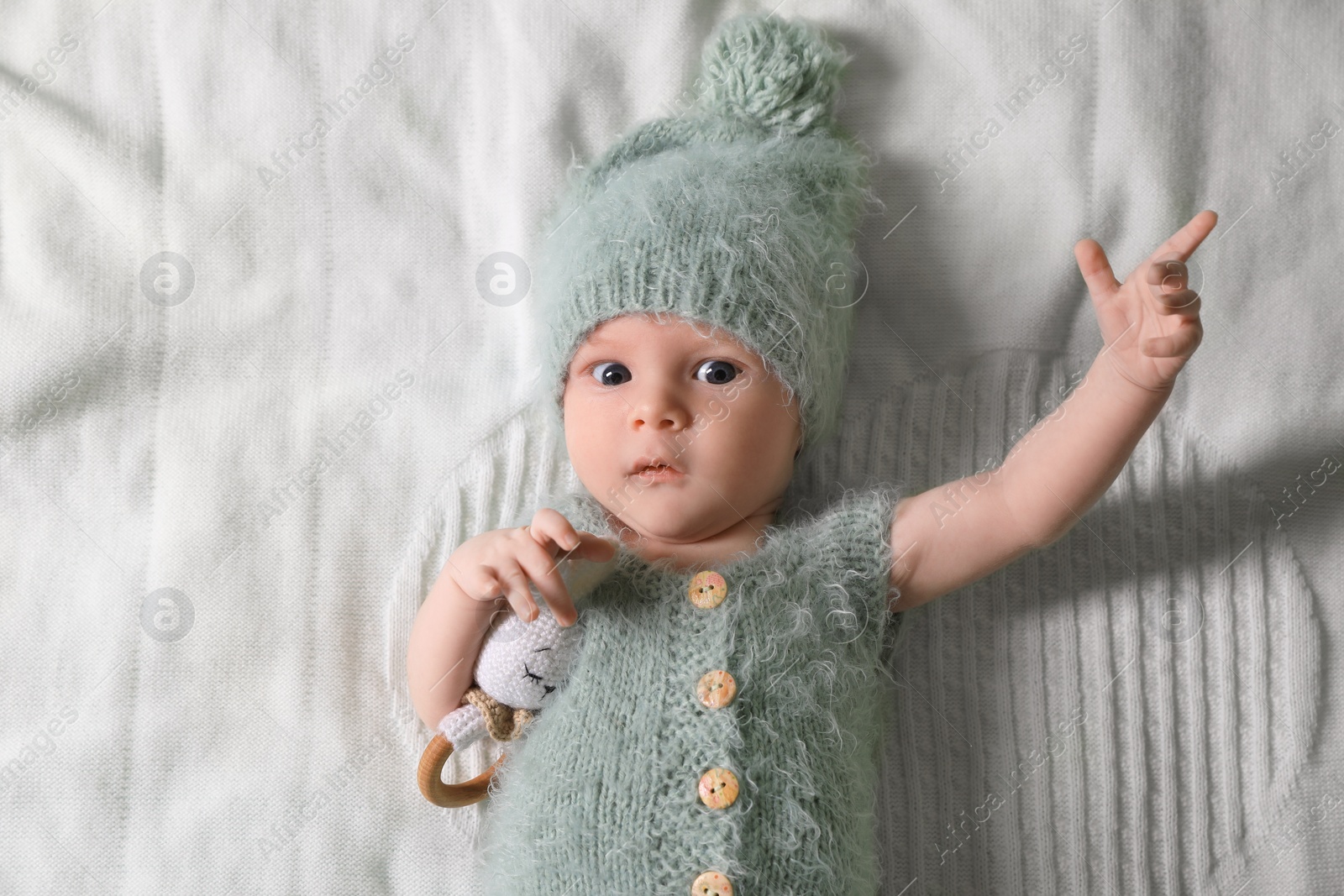 Photo of Cute newborn baby with teething toy on white blanket, top view