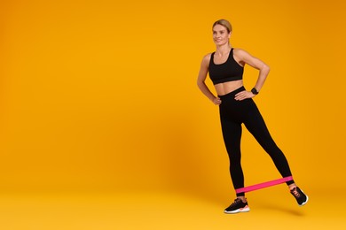Photo of Woman exercising with elastic resistance band on orange background. Space for text
