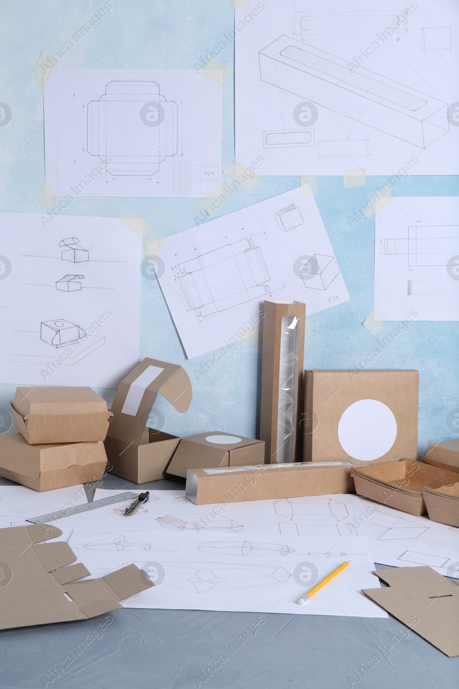 Photo of Creating packaging design. Drawings, boxes and stationery on blue textured table, closeup