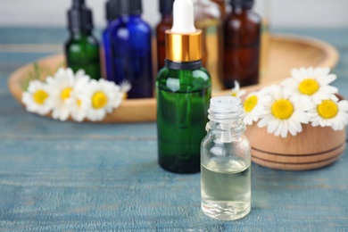 Photo of Bottles of chamomile essential oil and flowers on color table, space for text