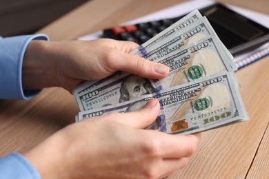 Money exchange. Woman counting dollar banknotes at wooden table, closeup