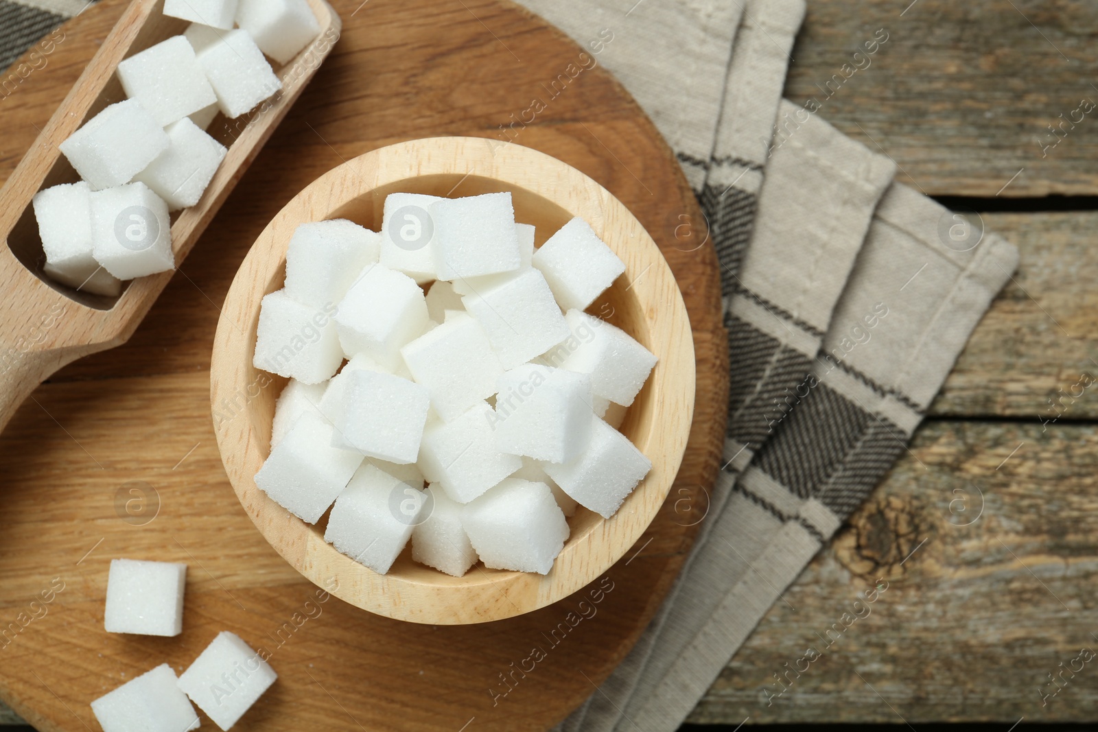 Photo of White sugar cubes in bowl and scoop on wooden table, top view