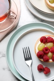 Photo of Delicious tartlet with berries and tea on white marble table, flat lay