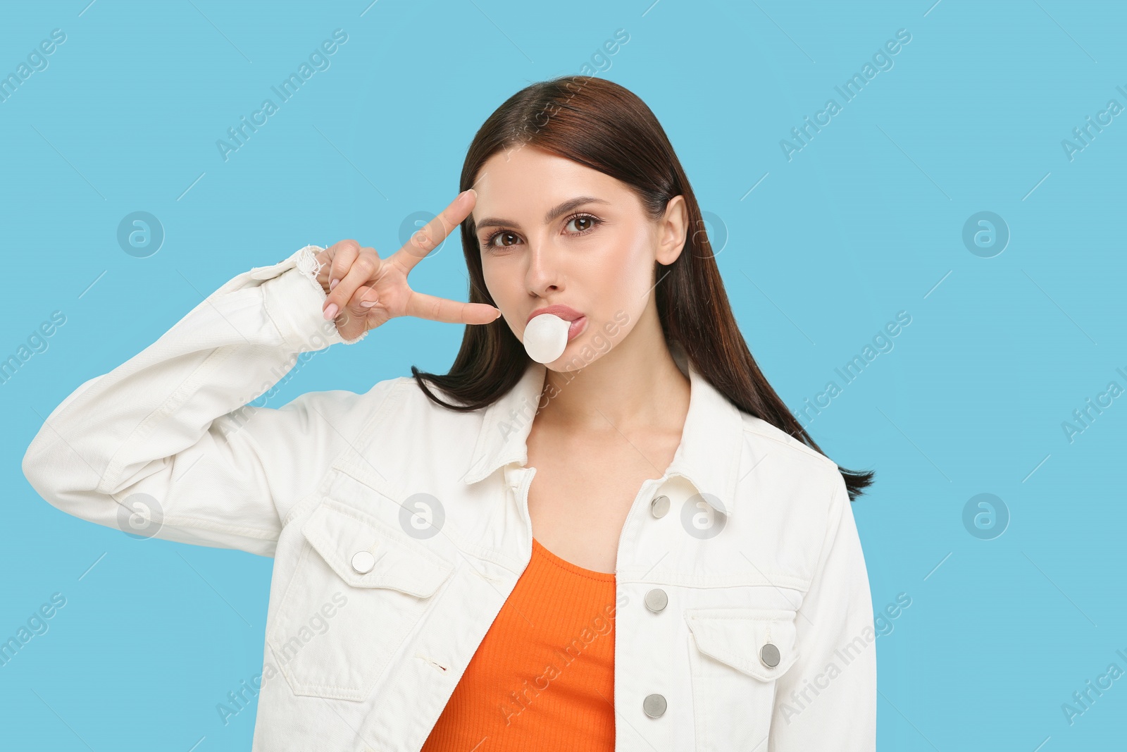 Photo of Beautiful woman blowing bubble gum and gesturing on light blue background