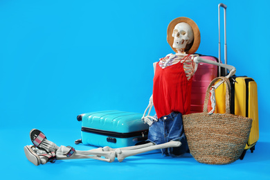 Photo of Human skeleton in summer clothes with suitcases on blue background