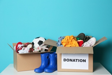 Photo of Donation boxes with clothes, shoes and toys on table against color background