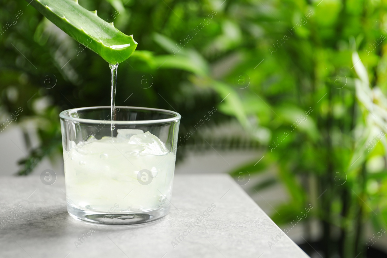 Photo of Aloe vera juice dripping from leaf into glass on table against blurred background with space for text