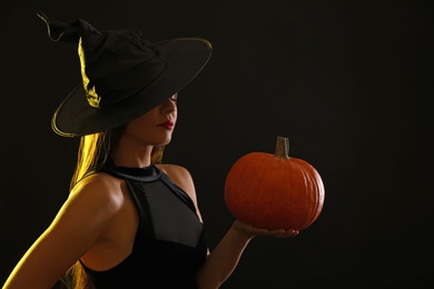 Photo of Young woman wearing witch costume with pumpkin on black background. Halloween party