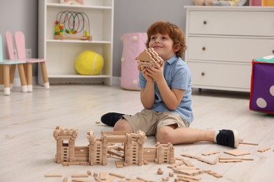 Photo of Little boy playing with wooden construction set on floor in room. Child's toy