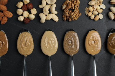 Photo of Tasty nut butters in spoons and raw nuts on dark gray textured table, flat lay