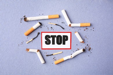 Photo of Card with word Stop, cigarette waste and burnt matches on light blue background, flat lay. Quitting smoking concept