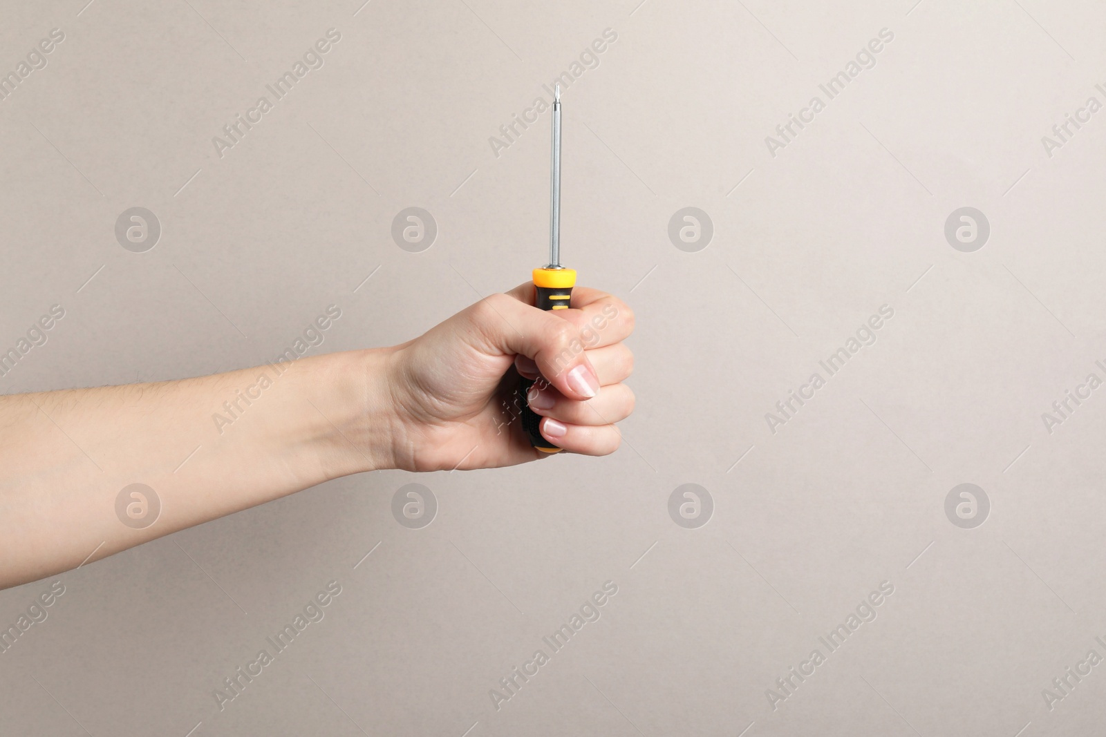 Photo of Woman holding screwdriver on grey background, closeup