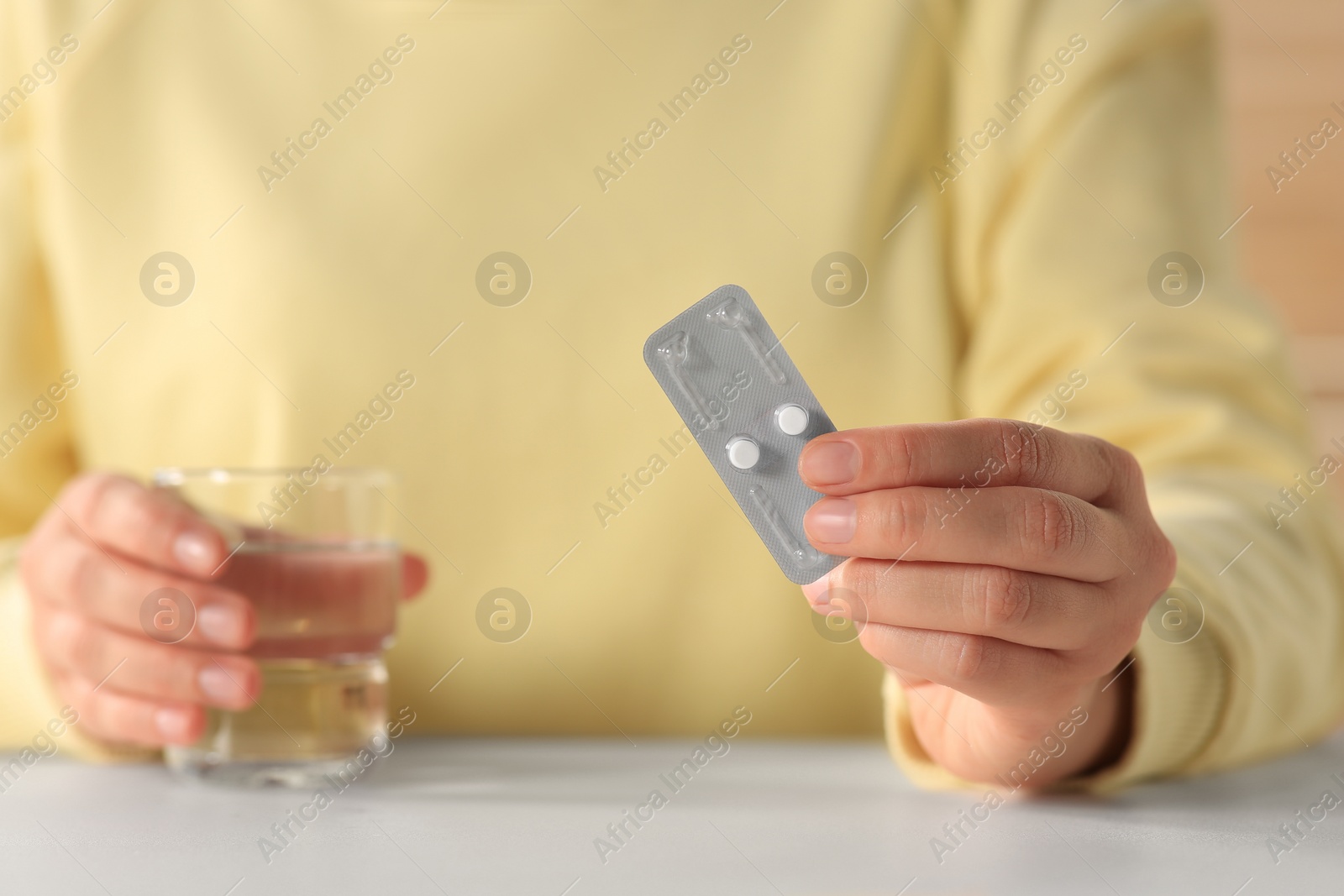 Photo of Woman taking emergency contraception pill at white table indoors, focus on hand