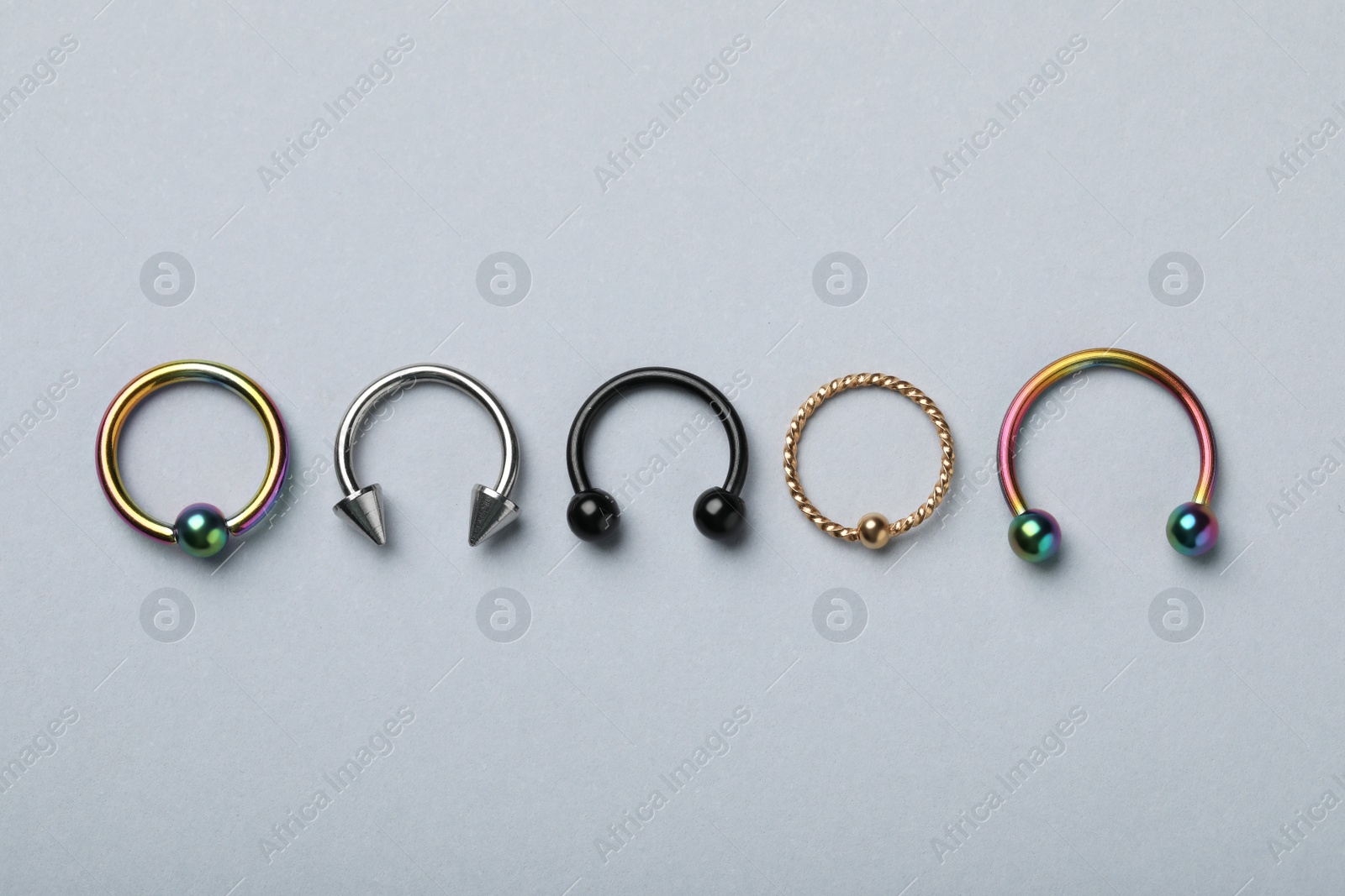 Photo of Stylish captive bead and horseshoe rings on light grey background, flat lay. Piercing jewelry