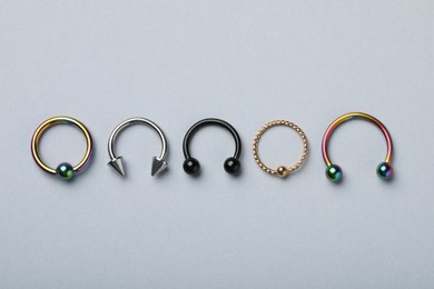 Stylish captive bead and horseshoe rings on light grey background, flat lay. Piercing jewelry