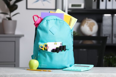 Turquoise backpack and different school stationery on table indoors