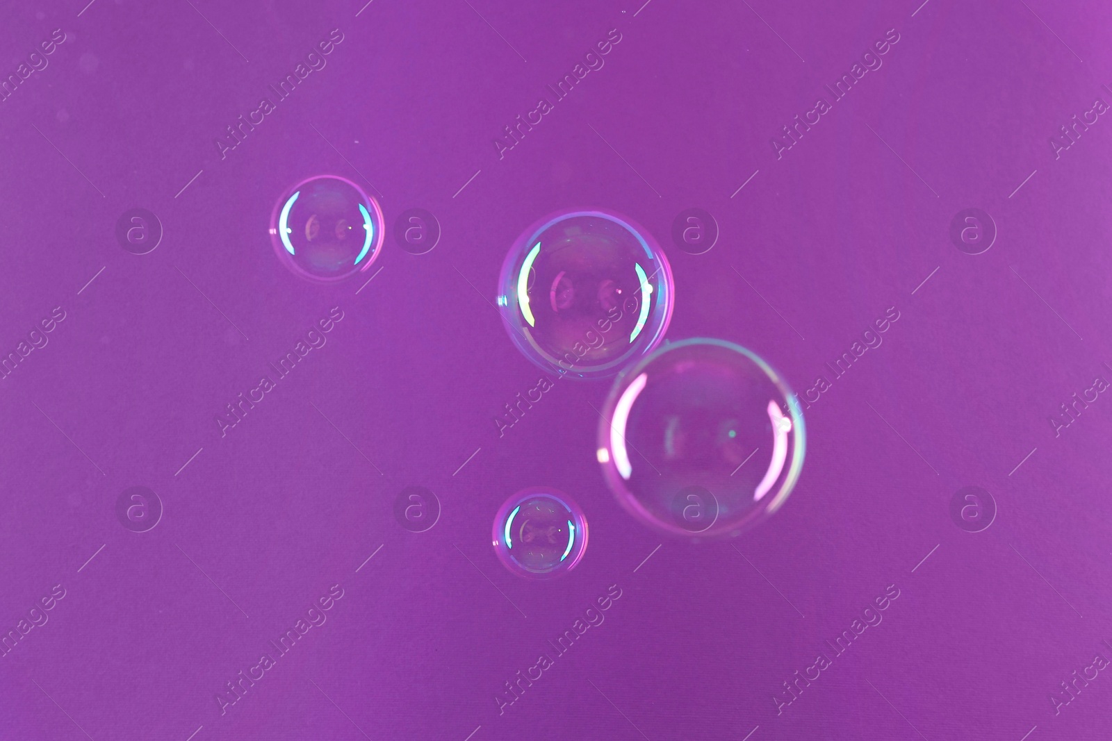 Photo of Beautiful transparent soap bubbles on violet background