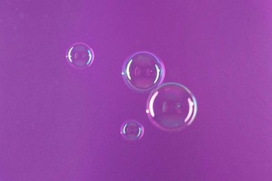 Photo of Beautiful transparent soap bubbles on violet background