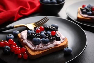 Photo of Tasty sandwiches with cream cheese and berries on black plate, closeup