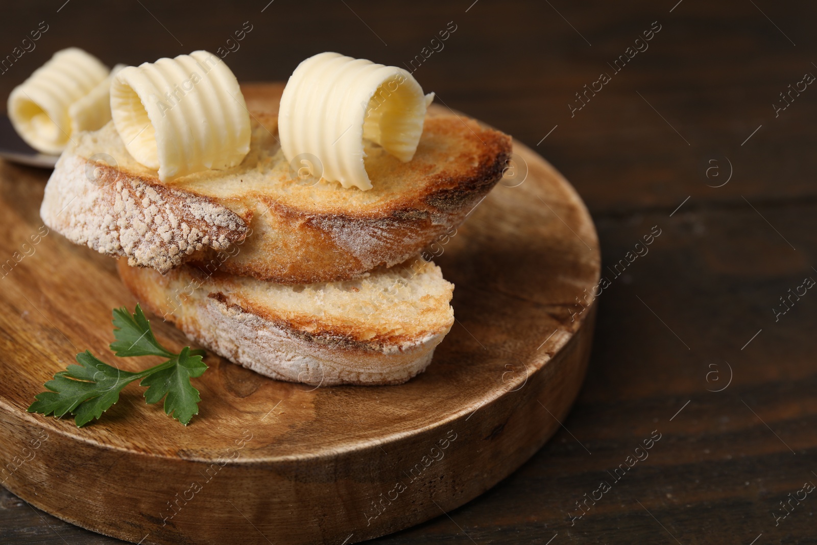 Photo of Tasty butter curls and slices of bread on wooden table, closeup