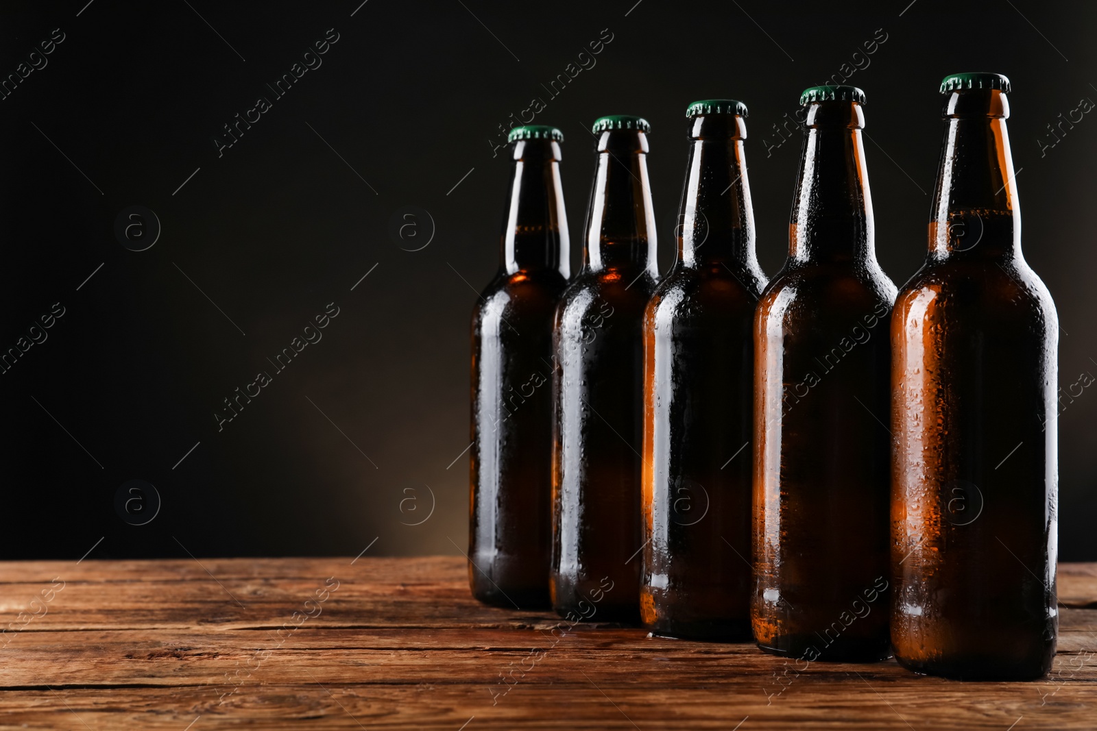 Photo of Many bottles of beer on wooden table against dark background, space for text