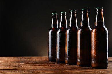 Photo of Many bottles of beer on wooden table against dark background, space for text
