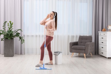 Photo of Enjoying cleaning. Happy woman in headphones listening music and mopping at home