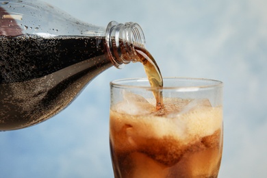Photo of Pouring refreshing soda drink into glass on blue background, closeup
