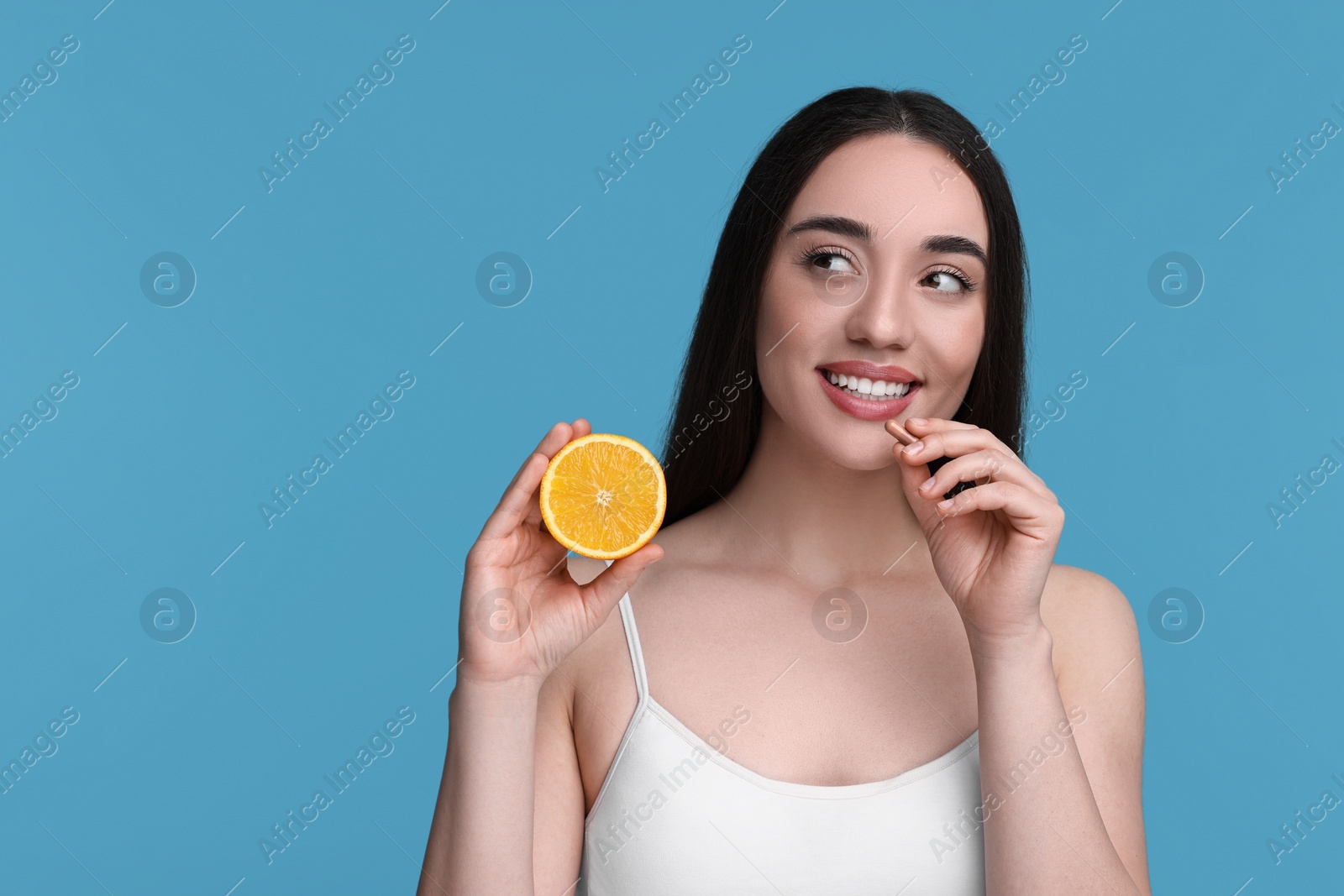 Photo of Beautiful young woman with vitamin pill and piece of orange on light blue background. Space for text