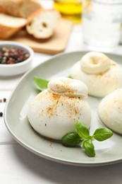 Photo of Delicious burrata cheese with basil on white wooden table, closeup