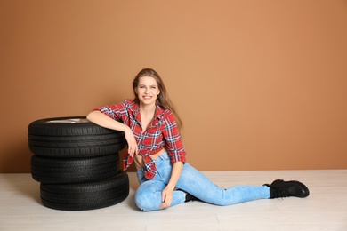 Young woman in seductive outfit with car tires on color wall background