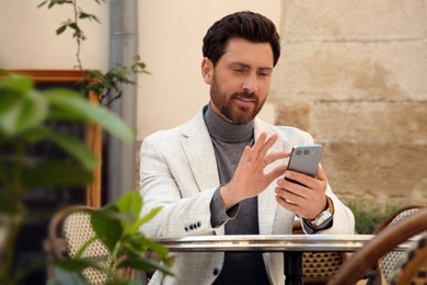 Handsome man sending message via smartphone at table outdoors