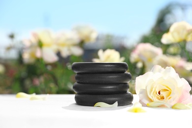 Photo of Stack of spa stones and beautiful rose on white table in blooming garden, space for text. Harmony and zen