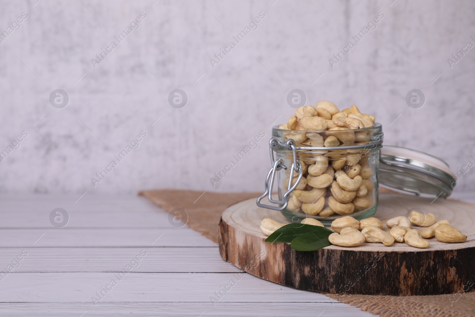 Photo of Glass jar with tasty cashew nuts on white wooden table. space for text