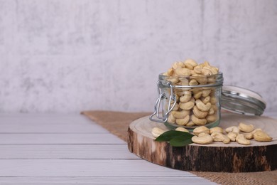 Photo of Glass jar with tasty cashew nuts on white wooden table. space for text