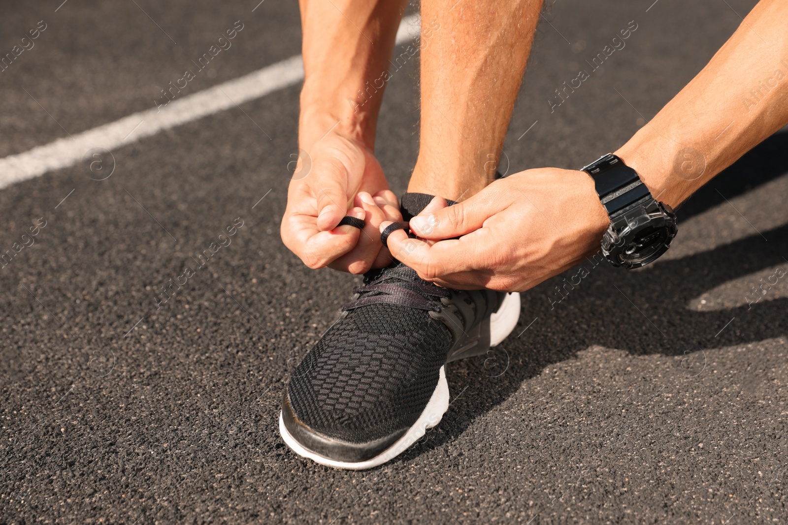 Photo of Young man tying shoelaces at stadium on sunny day