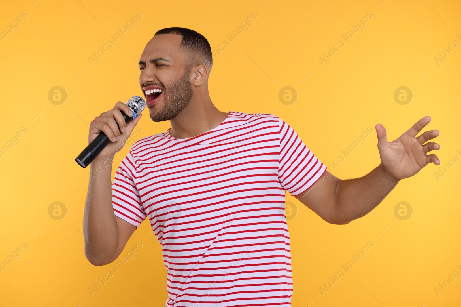 Photo of Handsome man with microphone singing on orange background