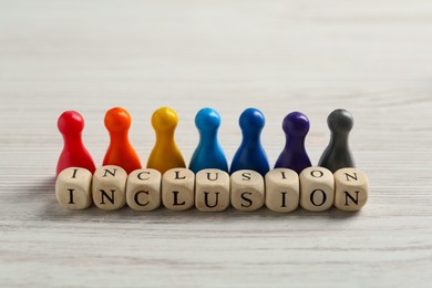 Photo of Colorful pawns and cubes with word Inclusion on white wooden table