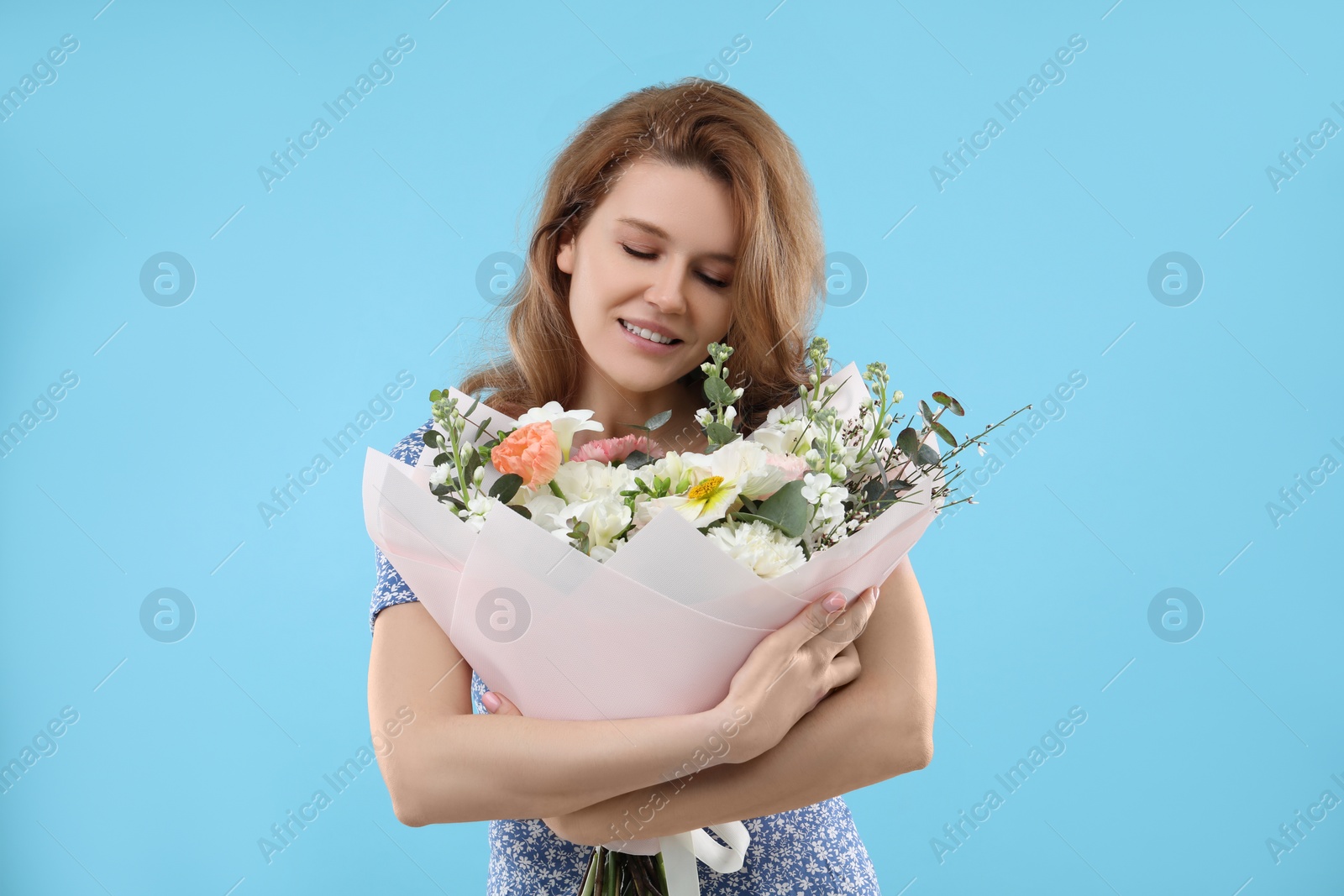 Photo of Happy woman with bouquet of beautiful flowers on light blue background