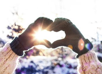 Young woman making heart with hands outdoors, closeup. Winter vacation